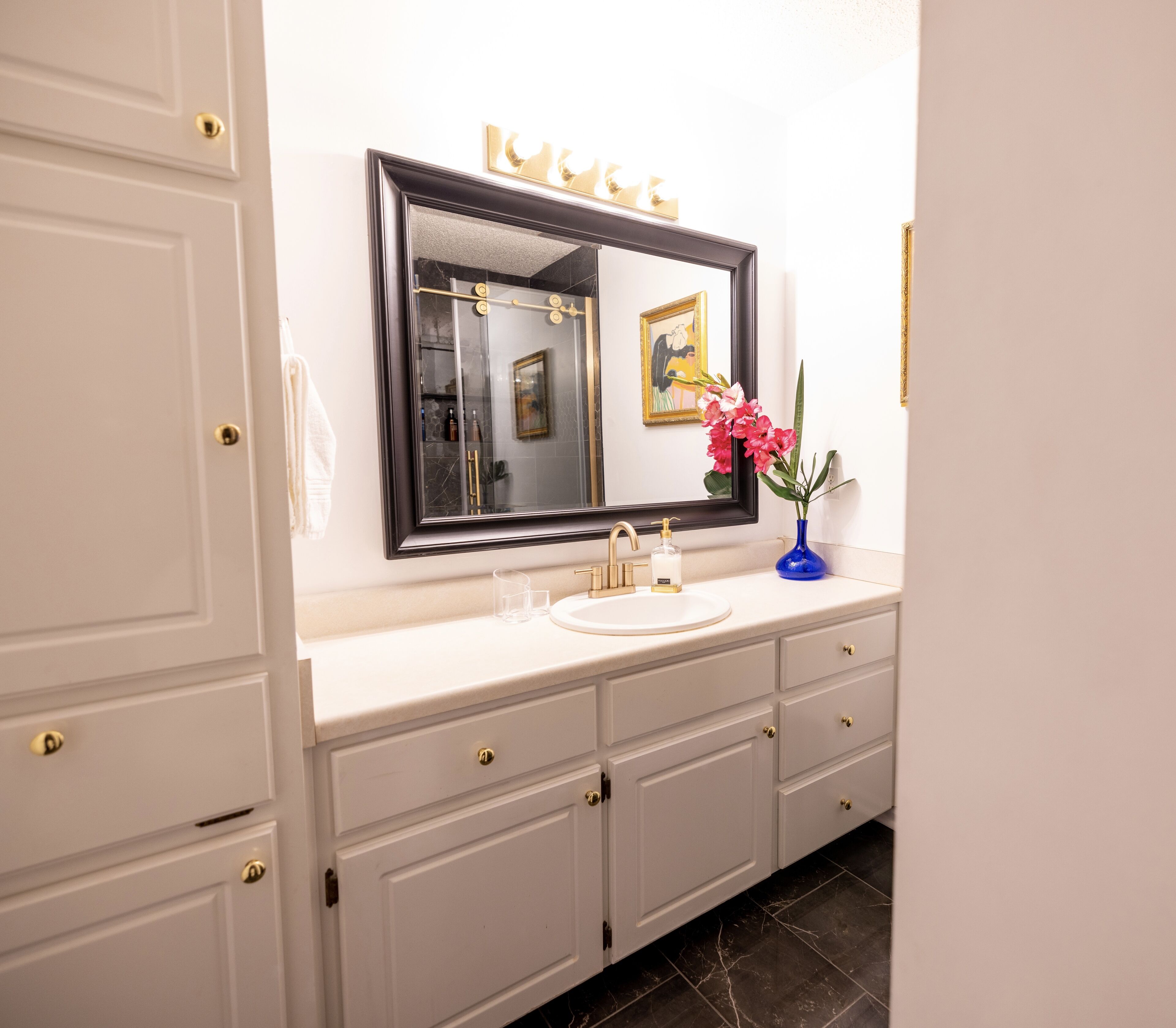 A bathroom with white cabinetry, a large mirror, a sink, and a vase with flowers.