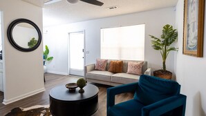 A modern living room with a sofa, a blue armchair, a coffee table, a ceiling fan, and a large window.