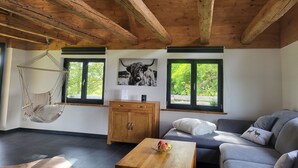Une pièce chaleureuse avec un plafond en bois, un fauteuil suspendu, un canapé et une table sur laquelle sont posées des pommes.