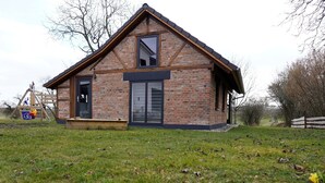 Une maison en briques avec un toit à pignon, une porte d’entrée et une grande fenêtre.
