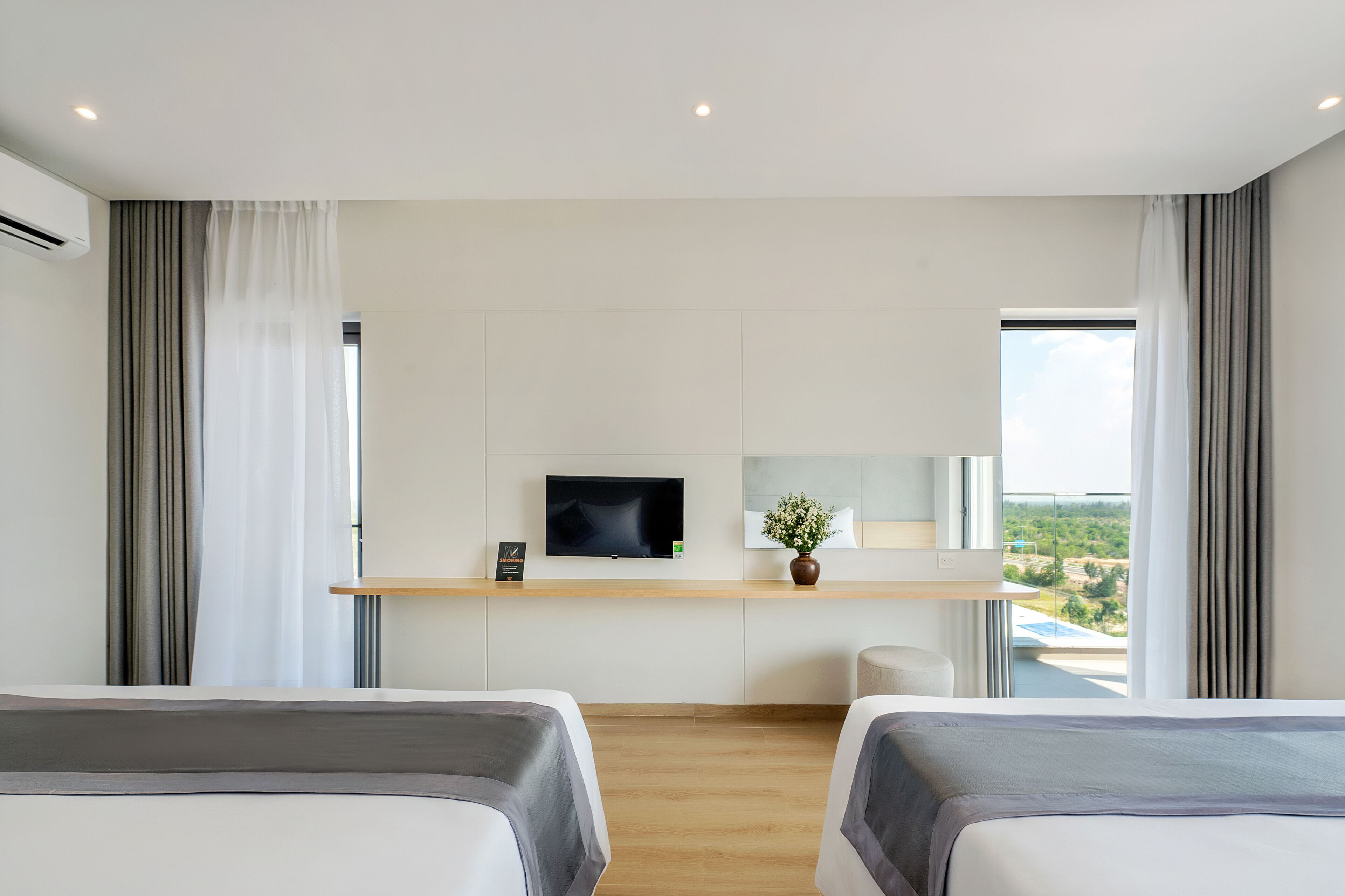 Habitación de hotel moderna con dos camas, un televisor, un escritorio pequeño y vistas al exterior.