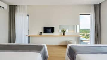 Habitación de hotel moderna con dos camas, un televisor, un escritorio pequeño y vistas al exterior.