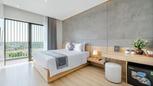 A modern hotel room with a large bed, a desk, a small stool, a nightstand, and a view of the city. - Thuan Hue Boutique Hotel - Nam Hoi An (Da Nang)