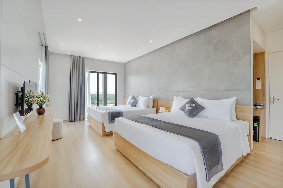 Quarto de hotel moderno com duas camas, uma escrivaninha e uma janela grande.