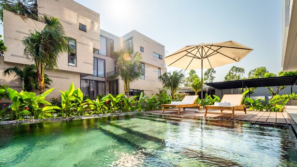 A modern pool area with clear water, surrounded by lush greenery and a contemporary building. - Thuan Hue Boutique Hotel - Nam Hoi An (Da Nang)