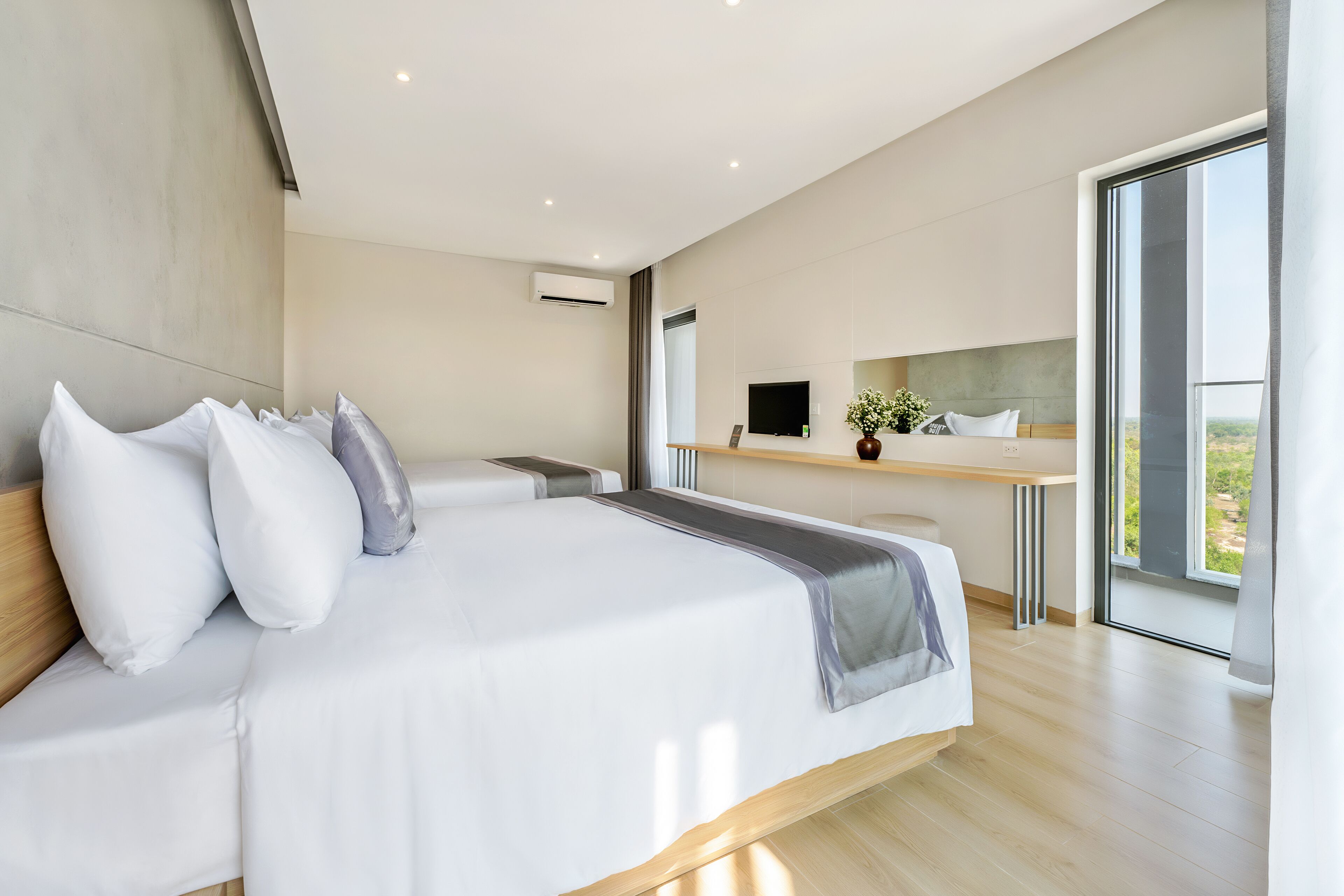 A modern hotel room with a large bed, a desk, and a large window offering a view.