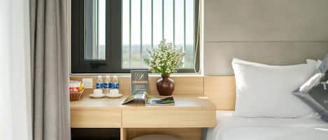 A hotel room with a bed, a desk with a vase of flowers, a window with blinds, and a sign prohibiting smoking.