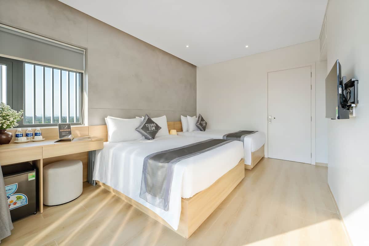 Quarto de hotel moderno com uma cama grande, uma escrivaninha, uma kitchenette pequena e uma janela ampla.