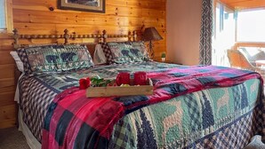 Ein Schlafzimmer einer Holzhütte mit Bett, einem gerahmten Bild an der Wand und einem Fenster mit Vorhängen.