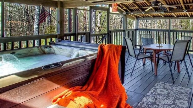 Ein Whirlpoolbereich mit Holzterrasse, überdachter Sitzecke und Blick auf Bäume durch die Fenster.