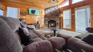 Ein gemütliches Blockhaus-Interieur mit Kamin aus Stein, Holzwänden, Deckenventilator und Fernseher.