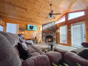 Een gezellig blokhutinterieur met een stenen openhaard, houten wanden, een plafondventilator en een televisie.