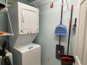 A laundry room with a front-loading washer and dryer, a mop, and a broom.
