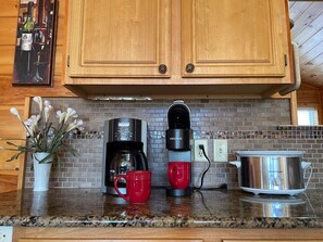 Una cucina con mobili in legno, una macchina per il caffè, una tazza rossa, una slow cooker in acciaio inox e una pianta in vaso.