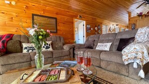 Ein gemütliches Blockhaus-Interieur mit Holzwänden, zwei Sofas, einem Couchtisch mit Snacks und Getränken sowie einer dekorativen Vase.