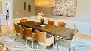 Un coin repas avec une table en bois, des chaises rembourrées, un luminaire suspendu et un tableau au mur.