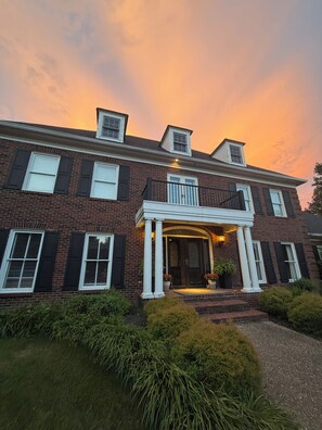 A two-story brick house with a front porch, a central entrance, and a small balcony. - Winner's Circle Derby Mansion (Prospect)