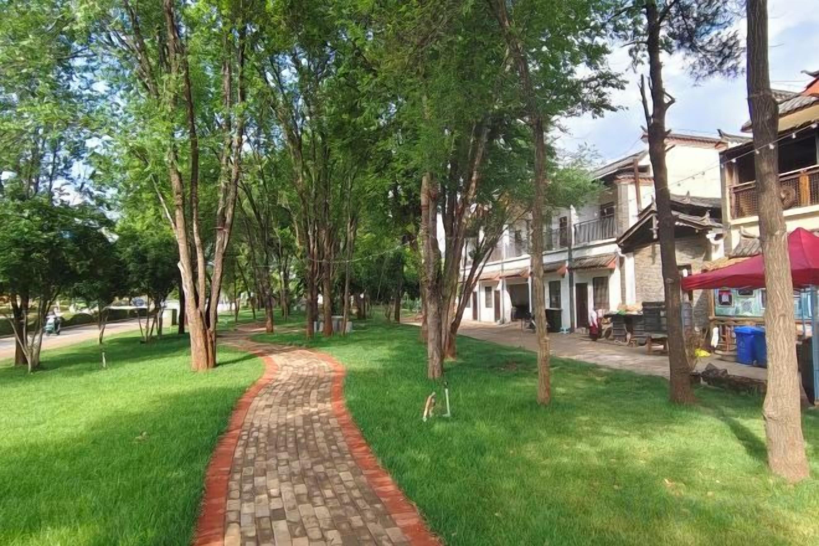 A pathway leading through a park with trees and buildings in the background.