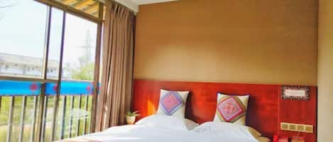 A hotel room with a large bed, a wooden ceiling, a view of a blue pool, and a red accent wall.