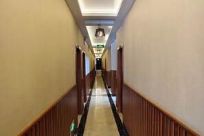 Un pasillo de hotel con paneles de madera, suelo de mármol y una lámpara en el techo.