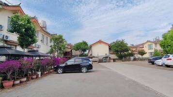 A residential street with parked cars, potted plants, and houses.