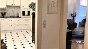 Un pasillo con una cocina a la izquierda, un interruptor de luz en la pared y un candelabro negro en la sala.