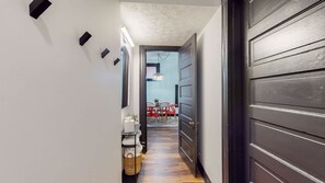 Un couloir doté d’un plancher en bois, d’une porte sombre et d’un coin repas avec des chaises rouges et une table.