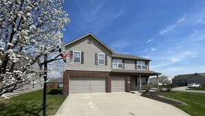 Une maison à deux étages avec un garage, un panier de basketball et une pelouse bien entretenue.