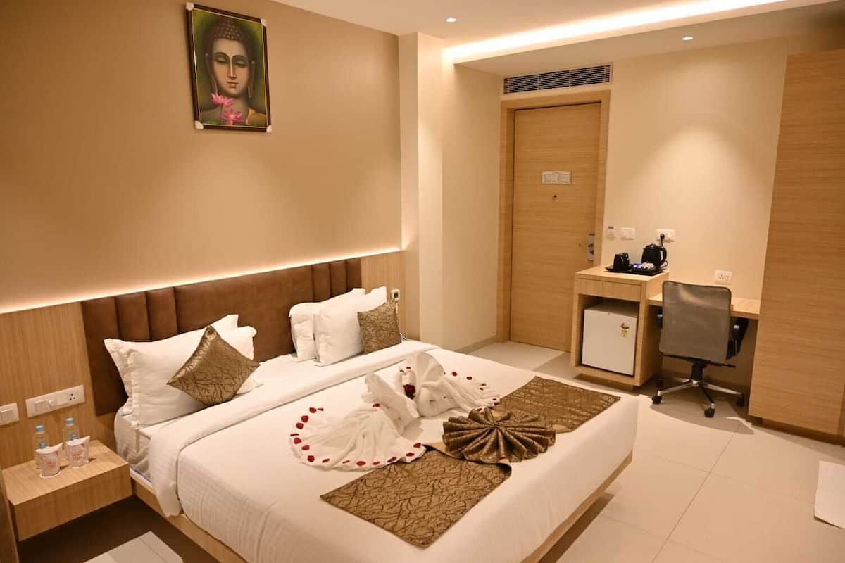 A hotel room with a bed, bedside table, desk, chair, and a painting on the wall.