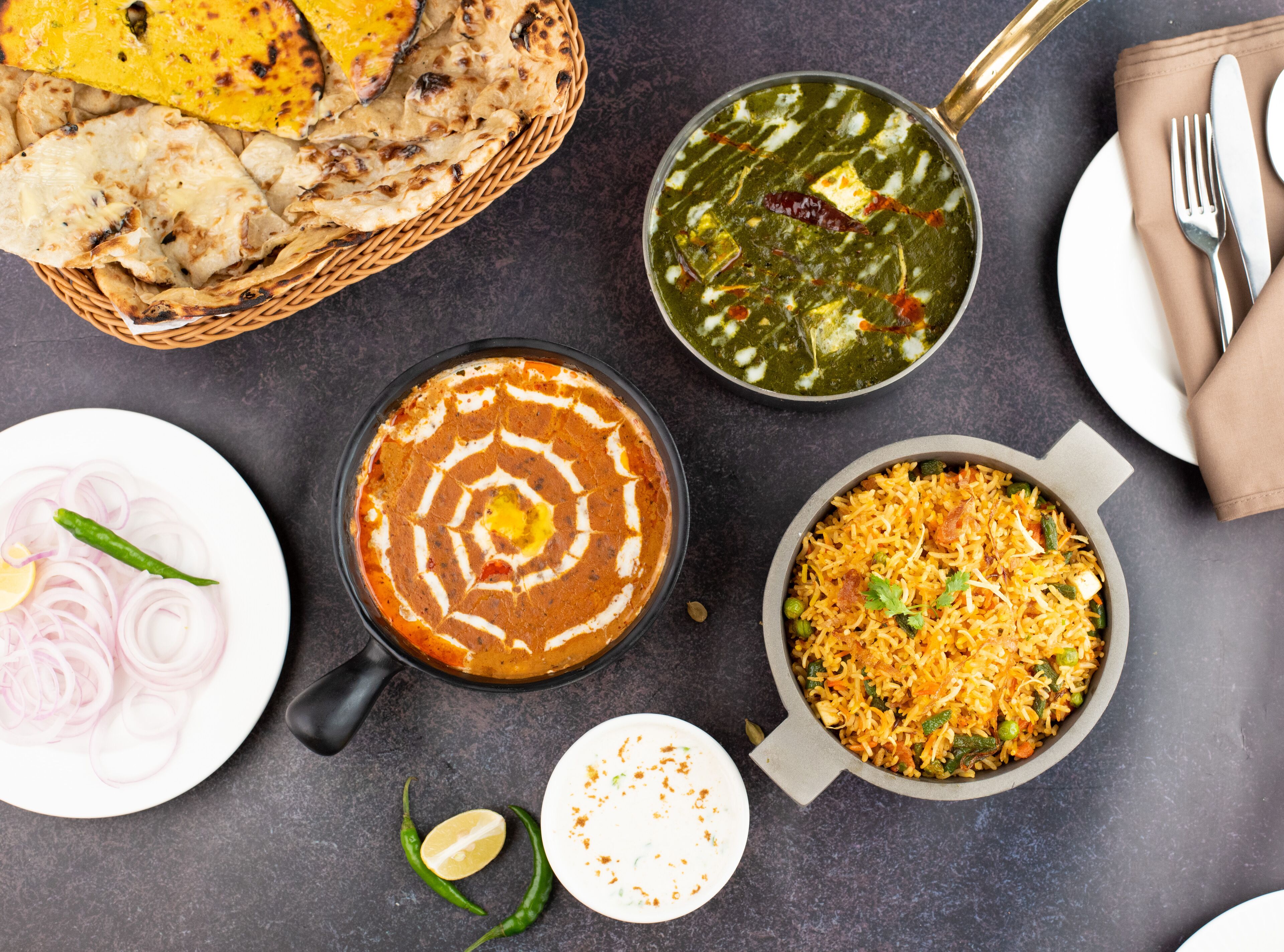 Une variété de plats indiens, notamment du pain naan, un bol de curry et une assiette d’oignons coupés en tranches.