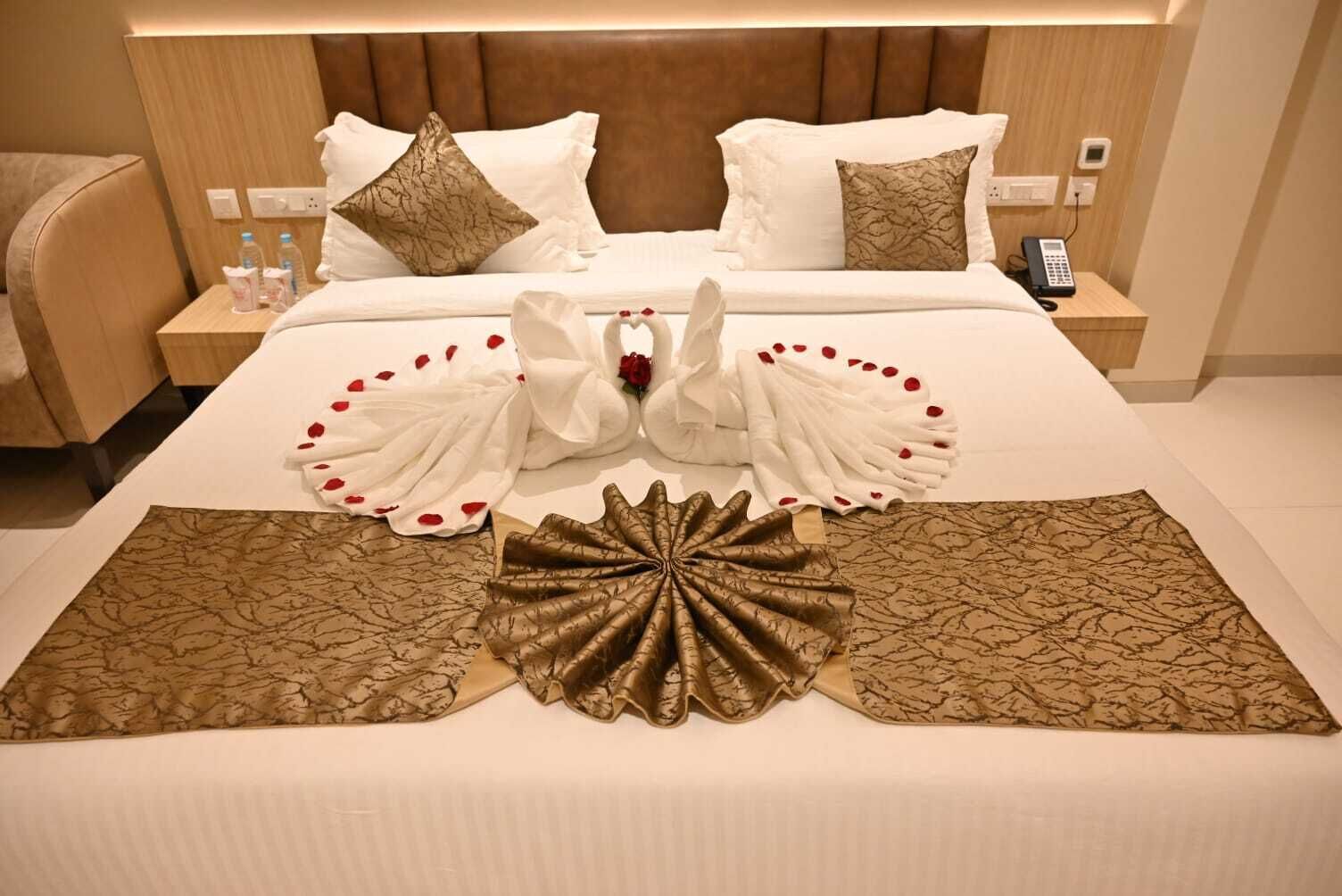 Quarto de hotel com uma cama bem arrumada, uma mesa de cabeceira com telefone e uma luminária.