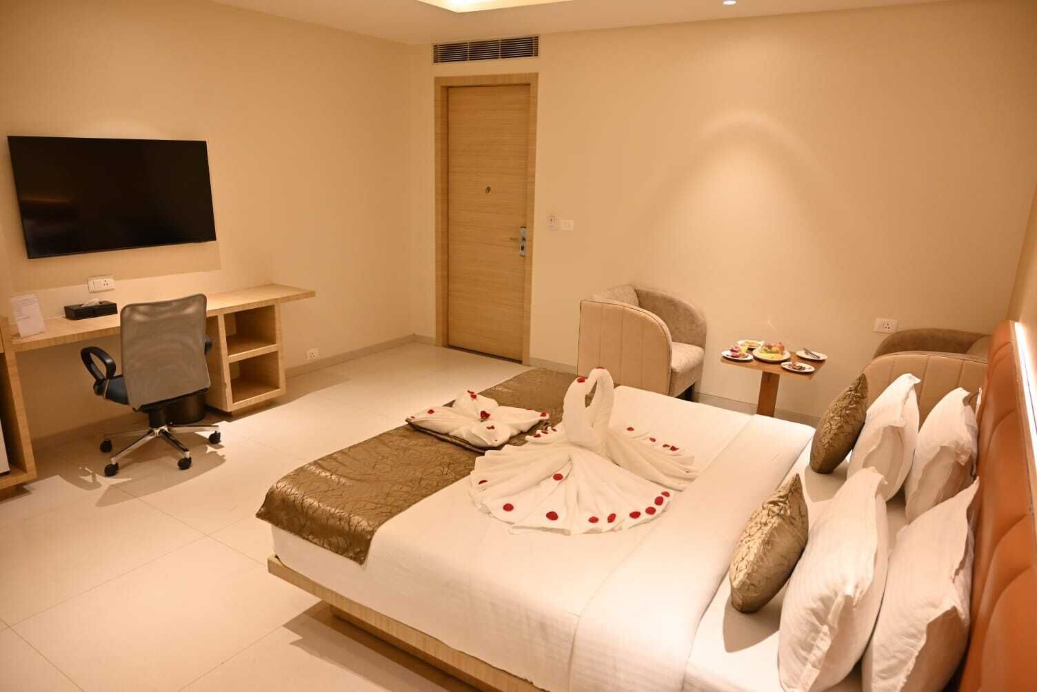 A hotel room with a bed, a desk, a chair, a TV, and a door.