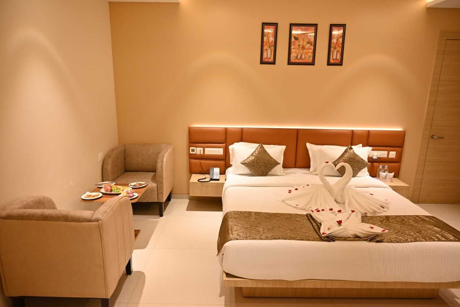 A hotel room with a bed, a chair, a bedside table with a phone, and a wall with three framed pictures.