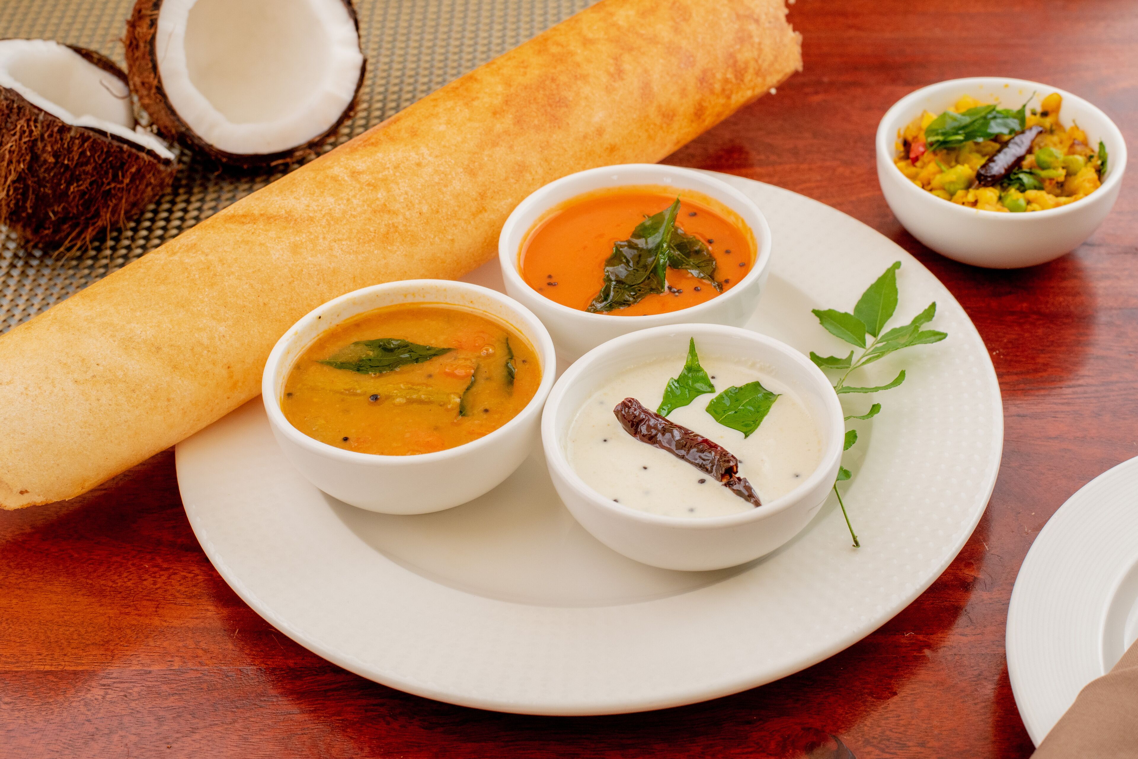 A plate with a rolled flatbread, two bowls of soup, and a small bowl of chutney.