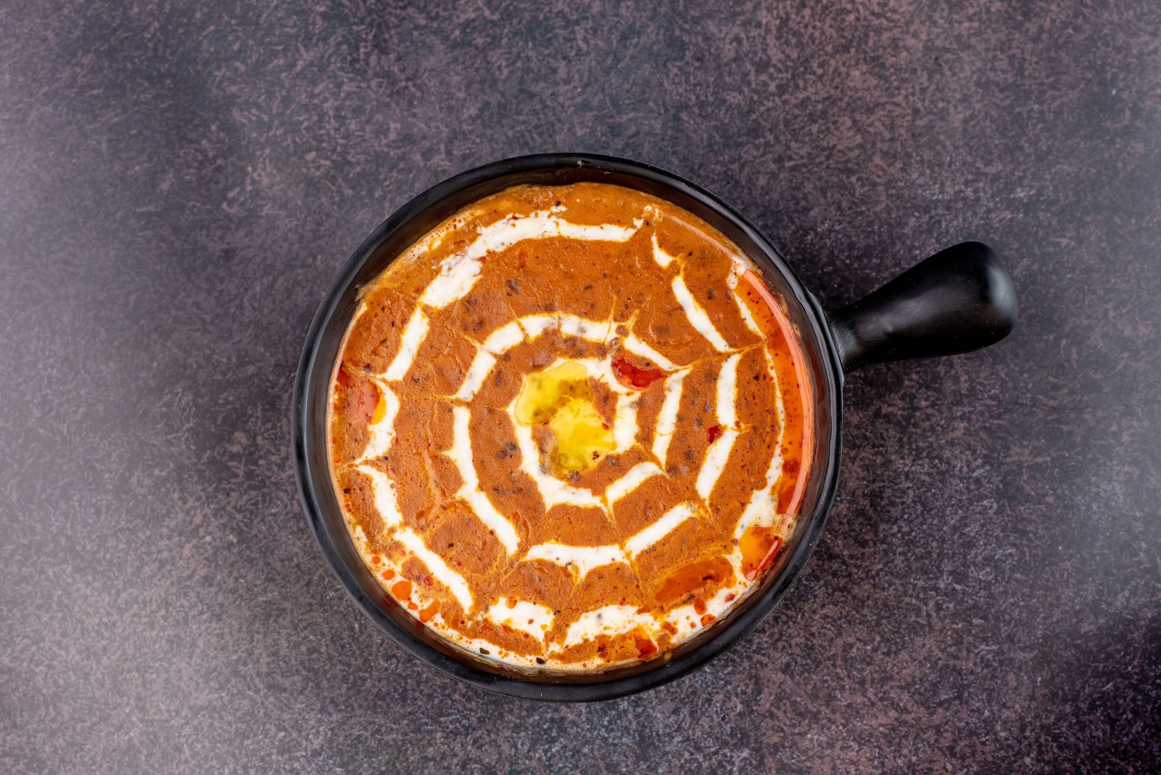 A bowl of curry with a decorative swirl pattern on a dark surface.