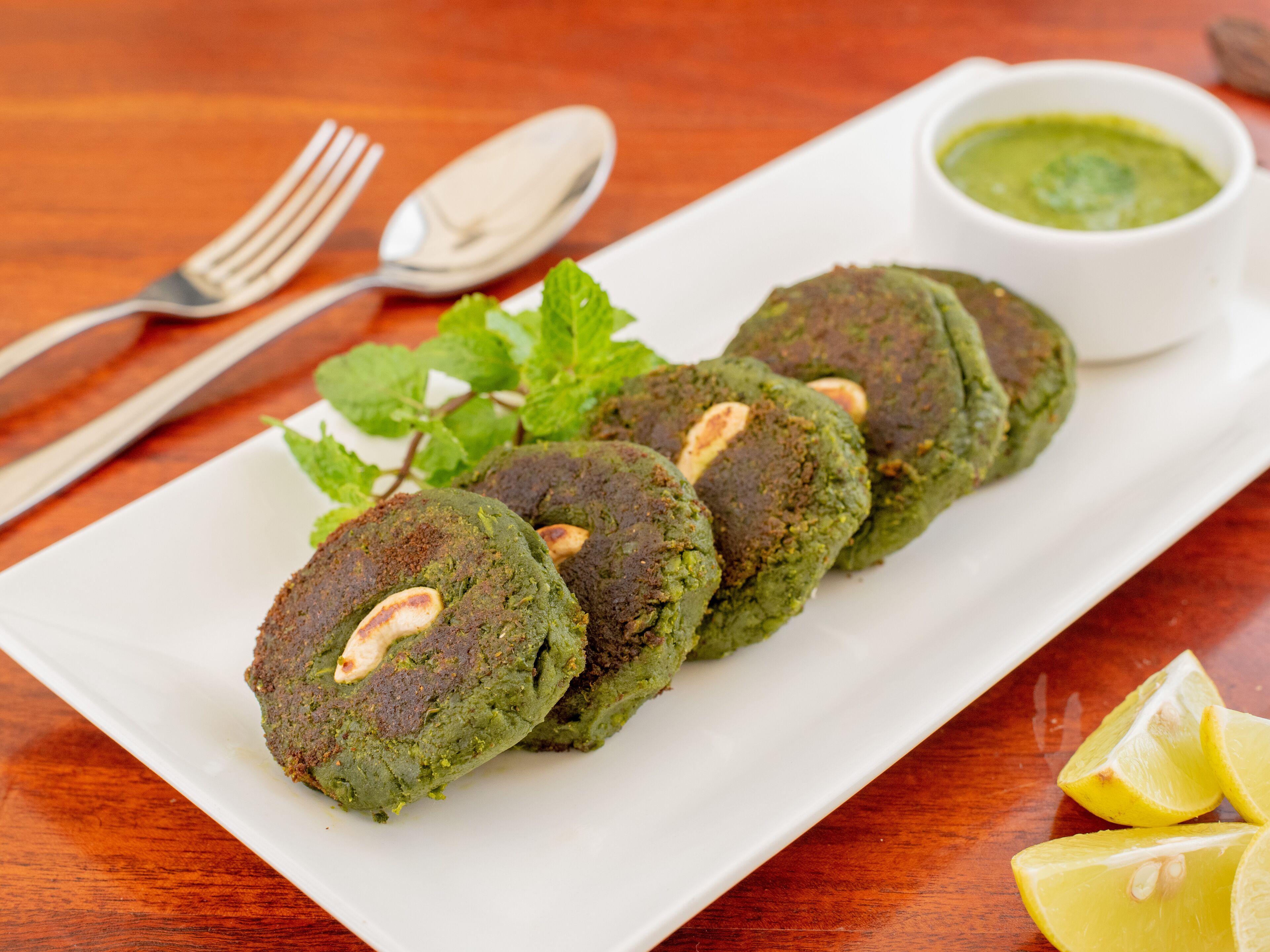 A plate of green patties with a side of green sauce and lemon wedges.