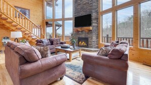 A spacious living room with leather sofas, a stone fireplace, and large windows. - Luxurious 4BD Lodge with HOT TUB! Fireplace! (Sevierville)