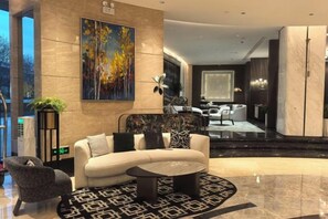 A modern lobby with a sofa, coffee table, and decorative pillows. There is a painting on the wall and a large window in the background.