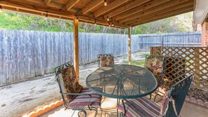 A covered patio area with a round metal table and chairs, a wooden ceiling, and a wooden fence in the background. - Hotty Toddy get away in Oxford! (Oxford)