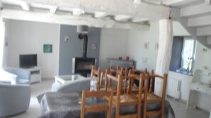 Ein Essbereich mit Holzkstühlen und einem Tisch, einem Fernseher und einem Kamin in einem Raum mit weißen Wänden und freiliegenden Balken.
