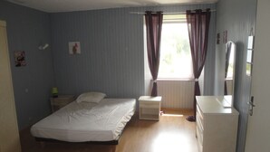 Ein Schlafzimmer mit einem Einzelbett, einem Nachttisch, einer Kommode und einem Fenster mit Vorhängen.