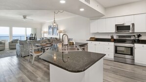 Una cocina moderna con armarios blancos, encimera de granito, electrodomésticos de acero inoxidable y vistas al océano.