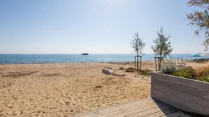 Ein Strand mit einer Holzterrasse, wolkenlosem Himmel und einem Schiffen im Hintergrund.