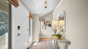 A hallway with a white door, a wooden floor, a mirror, and wall decor including plates and a lamp. - Pelican Place - Golf cart included 704 Swordfish (Fripp Island)