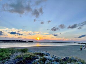 A beach scene with a sunset, rocky foreground, and a distant shoreline.
