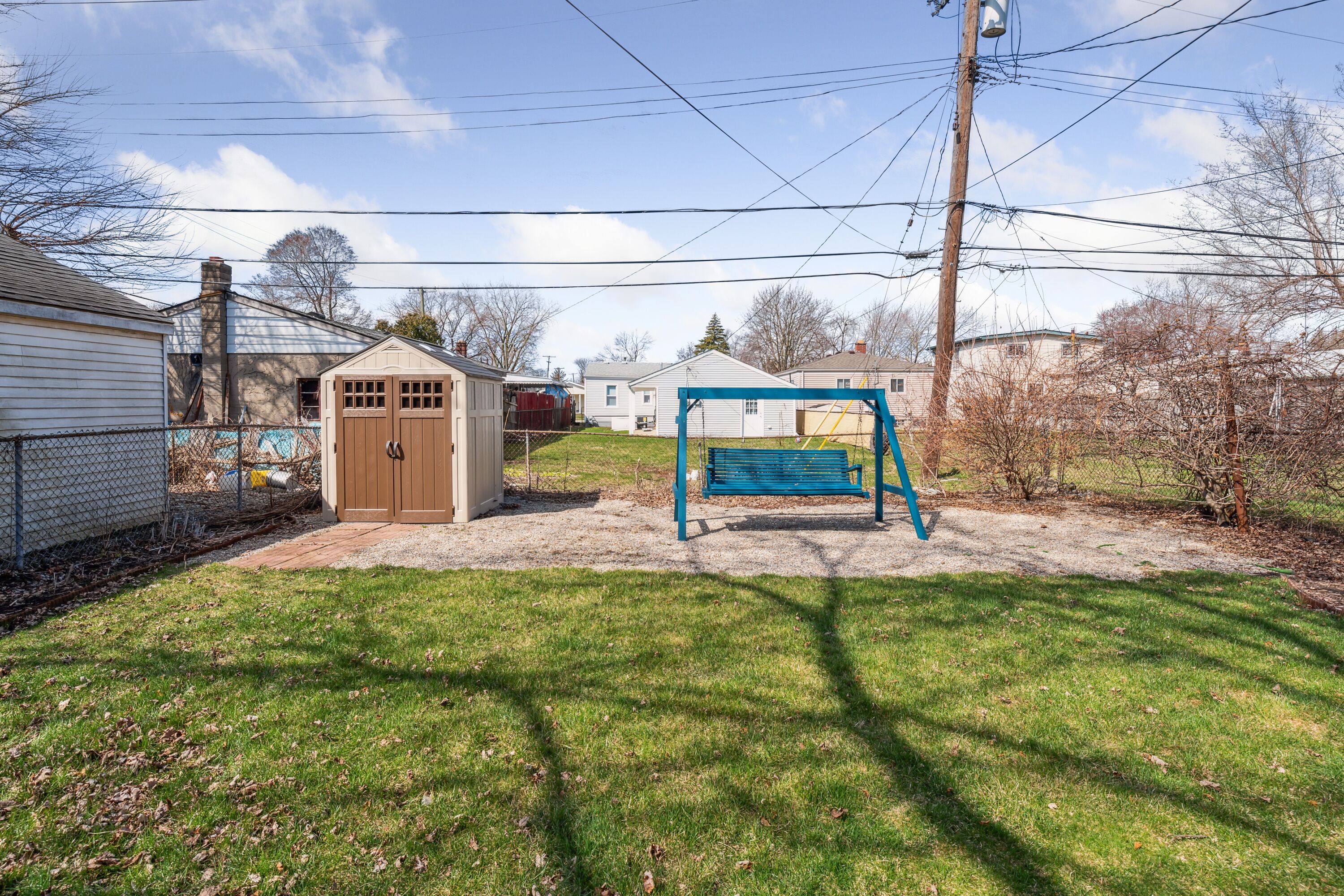 A backyard with a swing set, a shed, and a fenced area.