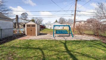 A backyard with a swing set, a shed, and a fenced area.