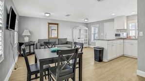 A modern kitchen with white cabinets, a dining area with a table and chairs, and a gray sofa. - Snowbirds save 50% Clean , pets, beachside apt. Downtown Flagler Beach -Sleeps 4 (Flagler Beach)