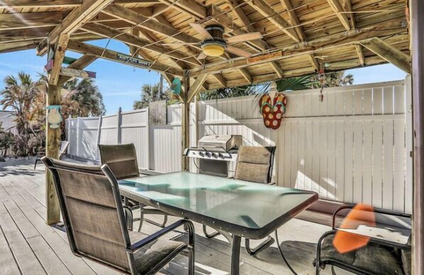 An outdoor patio with a wooden pergola, a glass-top table, metal chairs, and a grill.