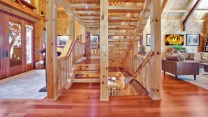 A wooden interior with a central staircase, wooden floors, and a living area with a sofa and a TV.